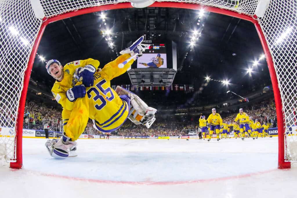 2017 IIHF Ice Hockey World Championship | Photography and video news, reviews and tips | Henry's Camera Hockey scene: yellow-clad goalie lunges to stop the puck near the net as teammates celebrate in the background.