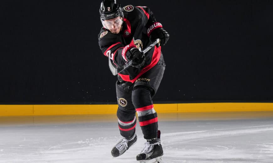 Ottawa Senators Production Day | Photography and video news, reviews and tips | Henry's Camera Hockey player in a black and red uniform skating forward on an indoor ice rink, gripping a stick as snow-like ice chips fly up.