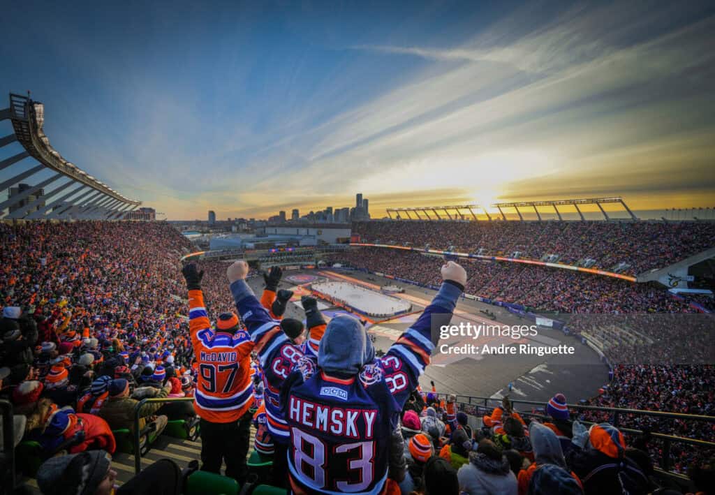 2023 Tim Hortons NHL Heritage Classic | Photography and video news, reviews and tips | Henry's Camera Fans in orange and blue jerseys cheer from the packed hockey arena as the sunset lights the city skyline in the background.