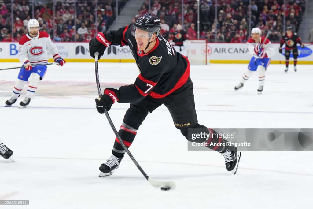 1 2026 445 | Photography and video news, reviews and tips | Henry's Camera Hockey player in a black and red jersey controls the puck during a fast-paced game on the ice online with a crowd in the background.