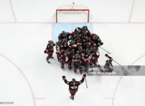 Overhead view of a hockey team celebrating in front of the net on an ice rink from above.