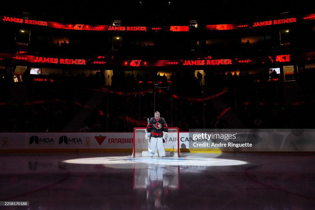 2 2026 436 | Photography and video news, reviews and tips | Henry's Camera Goaltender in front of the crease on a dark arena, spotlight on the ice and red LED boards reading 'James Reimer' and number 47 in the background.
