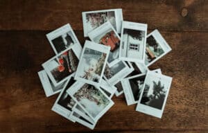 A pile of instant photo prints scattered on a dark wooden surface.