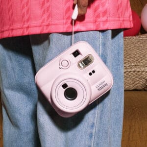 3Instax | Photography and video news, reviews and tips | Henry's Camera Pink Instax Mini 13 instant camera hanging from a strap against a person in a pink jacket and blue jeans.