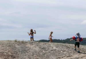 Children in swimsuits running on a rocky beach overlooking the sea under a cloudy sky.