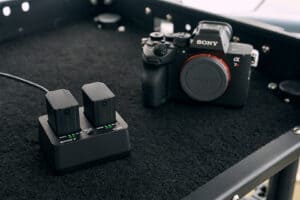 Sony Alpha camera on a black case with a dual-battery charger and two batteries in the foreground.
