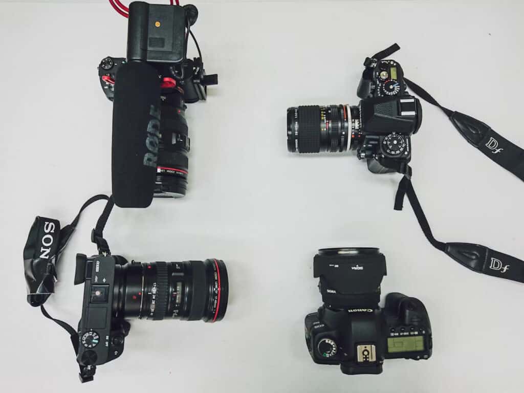 Cameras | Photography and video news, reviews and tips | Henry's Camera Four cameras laid out on a white surface in a square: top-left a large DSLR with a red-ring lens, top-right a DSLR with zoom lens, bottom-left a Sony camera with strap, bottom-right a Canon DSLR with lens cap on strap.