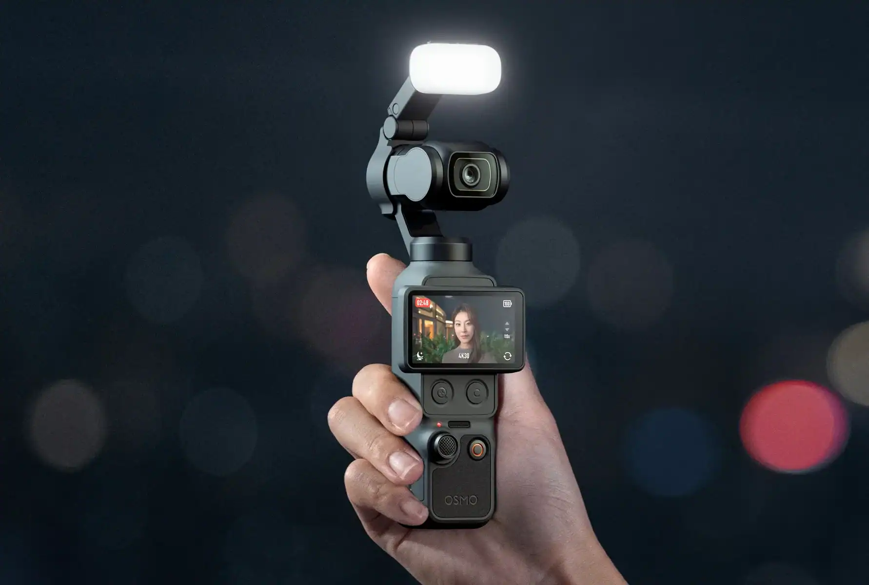 Handheld camera gimbal with a bright LED light on top, held against a dark, bokeh background.