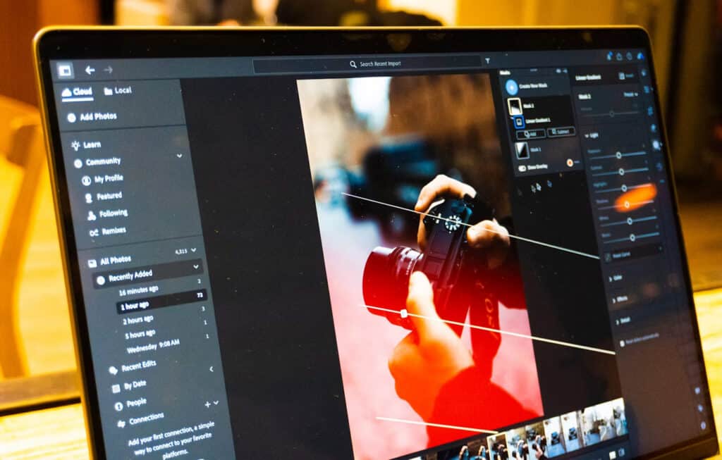 Editing | Photography and video news, reviews and tips | Henry's Camera Laptop screen displaying a photo-editing app with a red-tinted image of hands holding a camera; left and right tool panels visible, workflow in progress.
