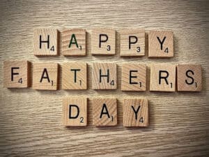 Wooden Scrabble tiles spell 'HAPPY FATHER'S DAY' on a light wood surface for a celebration message.