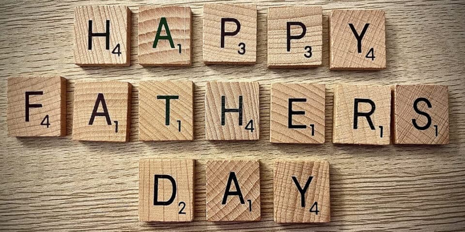 Wooden Scrabble tiles spell 'HAPPY FATHER'S DAY' on a light wood surface for a celebration message.