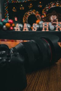 Close-up of a black DSLR with a large lens resting on a wooden table, stage with festive decorations blurred in the background.