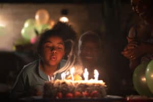 Low light photography - girl blowing out lit birthday candles on a cake
