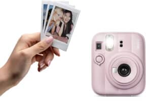 Pink Instax mini camera shown with a hand holding a small stack of Polaroid photos beside it for printing pictures now
