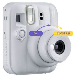 White Instax mini 13 camera close-up with an overlay showing arrows from ON to CLOSE UP, illustrating lens mode switch.