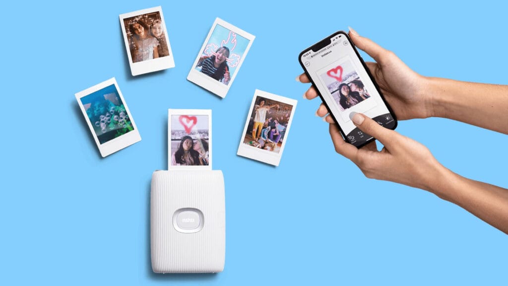 Instaxprinter | Photography and video news, reviews and tips | Henry's Camera White instax printer with several instant photos floating around against a blue background, and a hand holding a smartphone showing a printed photo