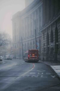 Red city bus seen from behind on a wet, foggy urban street lined with tall stone buildings and a 40 mph speed limit sign to the right.
