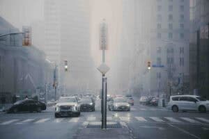 KN409596 | Photography and video news, reviews and tips | Henry's Camera City street intersection in foggy light with car traffic, traffic lights, and tall buildings in the background.