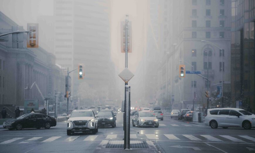 KN409596 | Photography and video news, reviews and tips | Henry's Camera City street intersection in foggy light with car traffic, traffic lights, and tall buildings in the background.