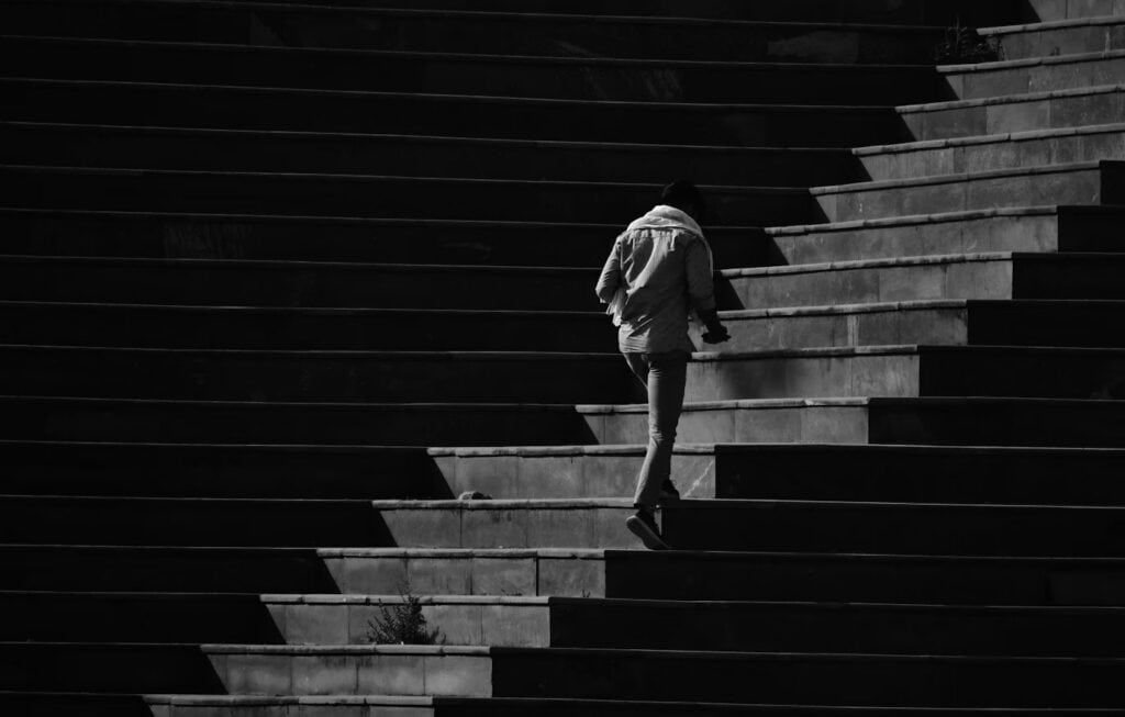 Leading-Lines | Photography and video news, reviews and tips | Henry's Camera Person seen from behind, walking up a flight of concrete outdoor stairs wearing a light jacket.
