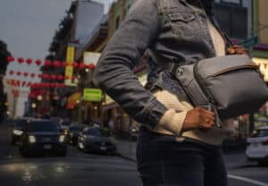 Peak-Design | Photography and video news, reviews and tips | Henry's Camera Person in a denim jacket and beige knit sweater wears a gray crossbody bag on a busy urban street.
