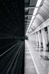 Empty underground subway platform with tracks curving into a dark tunnel on the left and a bright, curved wall on the right.