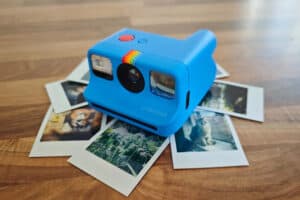 Polaroid2 | Photography and video news, reviews and tips | Henry's Camera Blue Polaroid instant camera resting on a spread of printed photos on a wooden table.