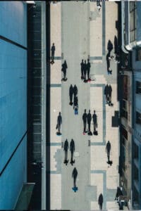 Aerial view of a urban pedestrian street between glass buildings with people walking and long shadows.