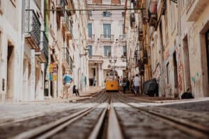 Yellow tram on a narrow city street with old buildings, pedestrians, and converging tram tracks in the foreground.
