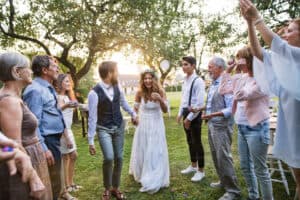 Wedding-Candid | Photography and video news, reviews and tips | Henry's Camera Bride and groom hold hands in a circle of cheering guests during an outdoor wedding in a sunny garden park.