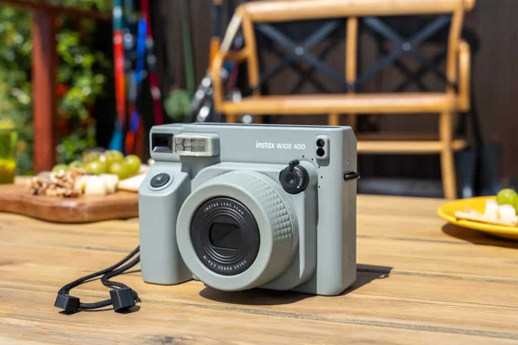 instaxwide | Photography and video news, reviews and tips | Henry's Camera Polaroid-style Instax Wide 400 instant camera on a wooden table with snacks and blurred garden backdrop in the background.