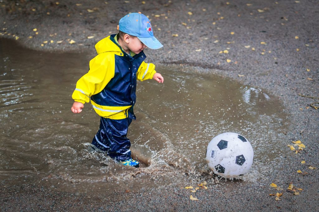 Little boy playing with soccer ball in puddle